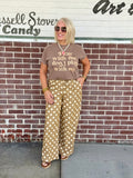 Unisex short sleeve brown shirt with 'Pray with Me Don't Play with Me' text, styled with patterned pants against a brick wall.