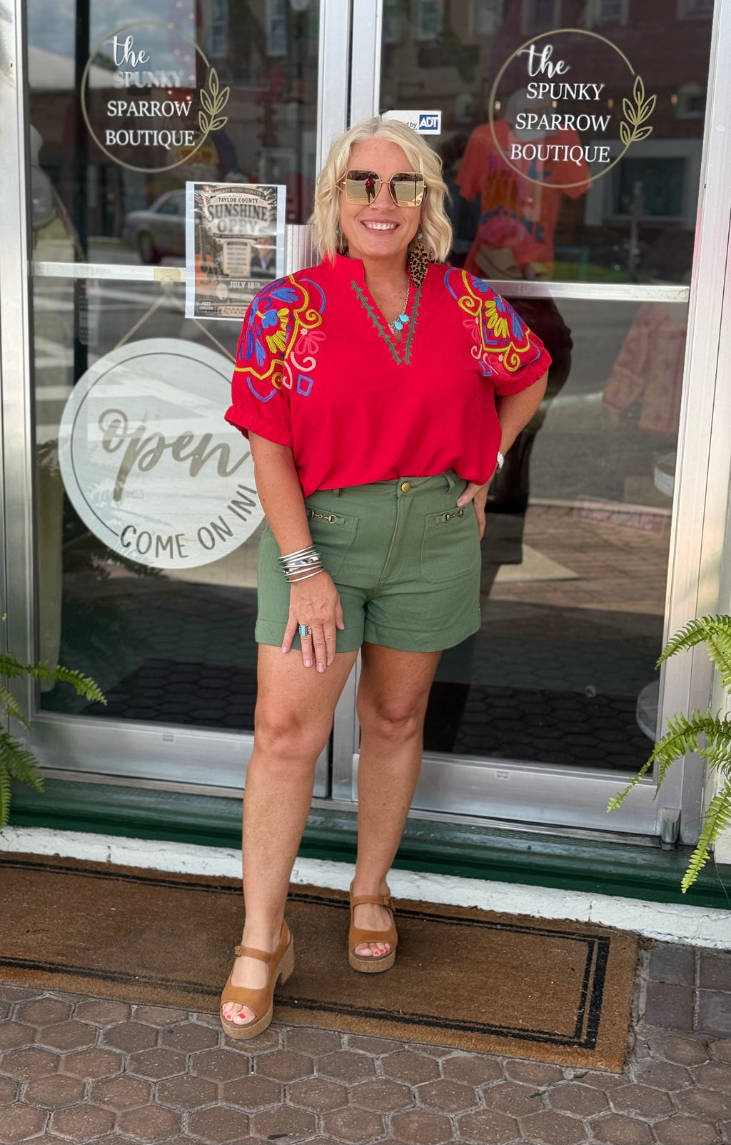 Vibrant tomato red blouse with split V-neck and multicolor embroidery, styled with green shorts and tan sandals.