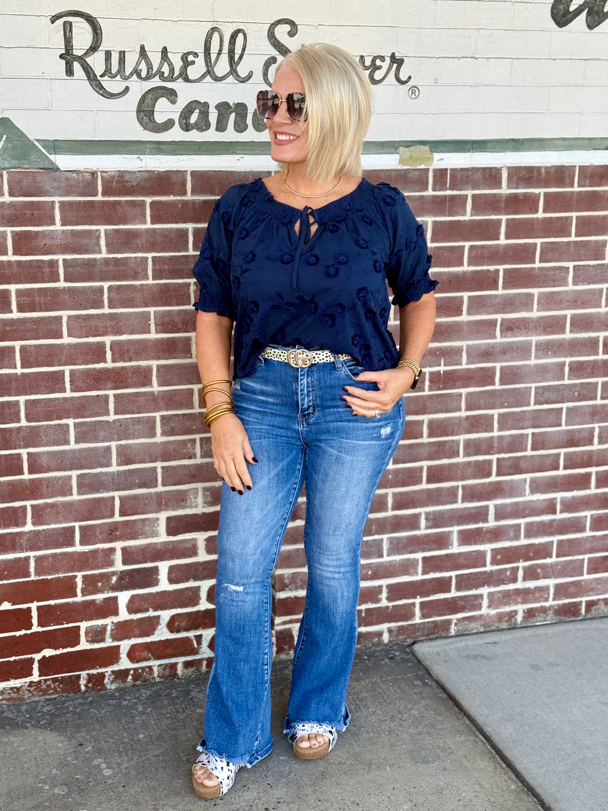 Navy blouse with 3D floral embroidery, featuring a boatneck neckline styled off the shoulder, paired with flared jeans.