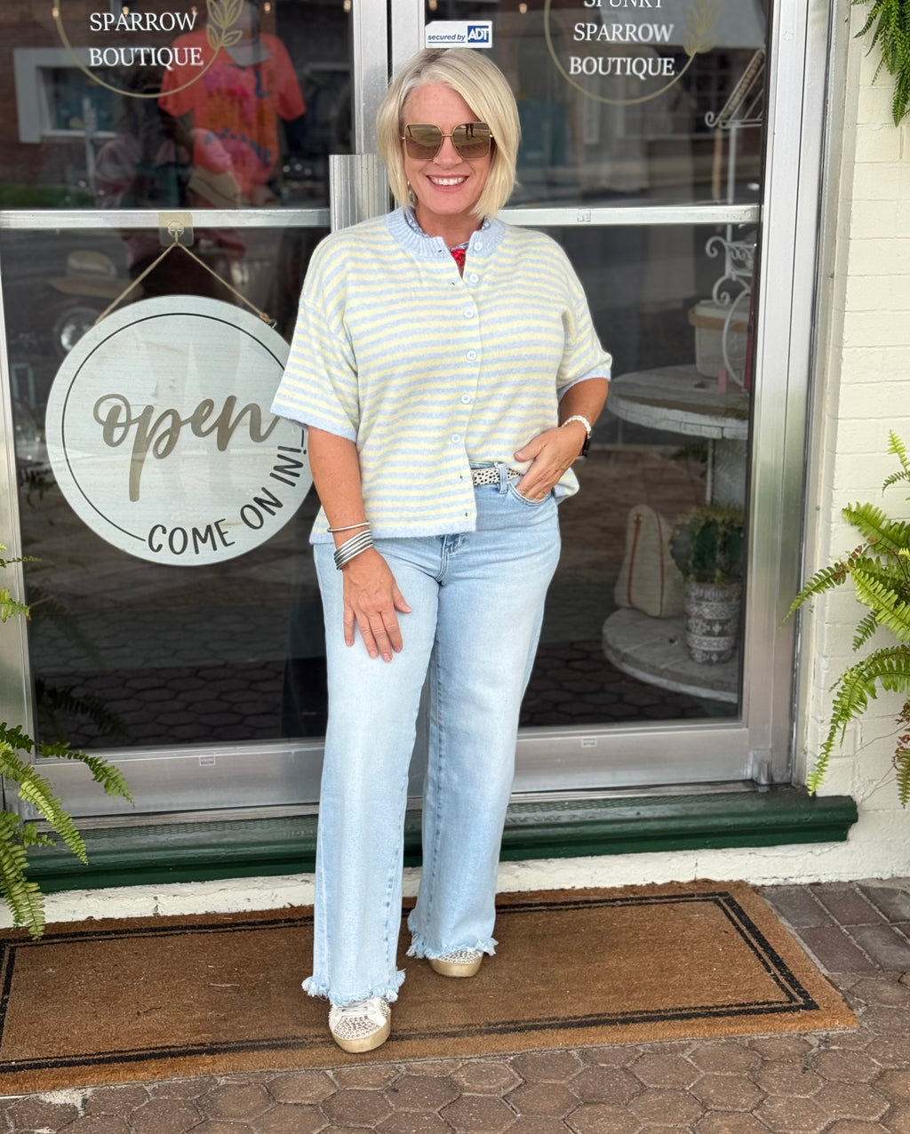Light blue and yellow striped short sleeve cardigan worn with light blue jeans in front of a boutique entrance.