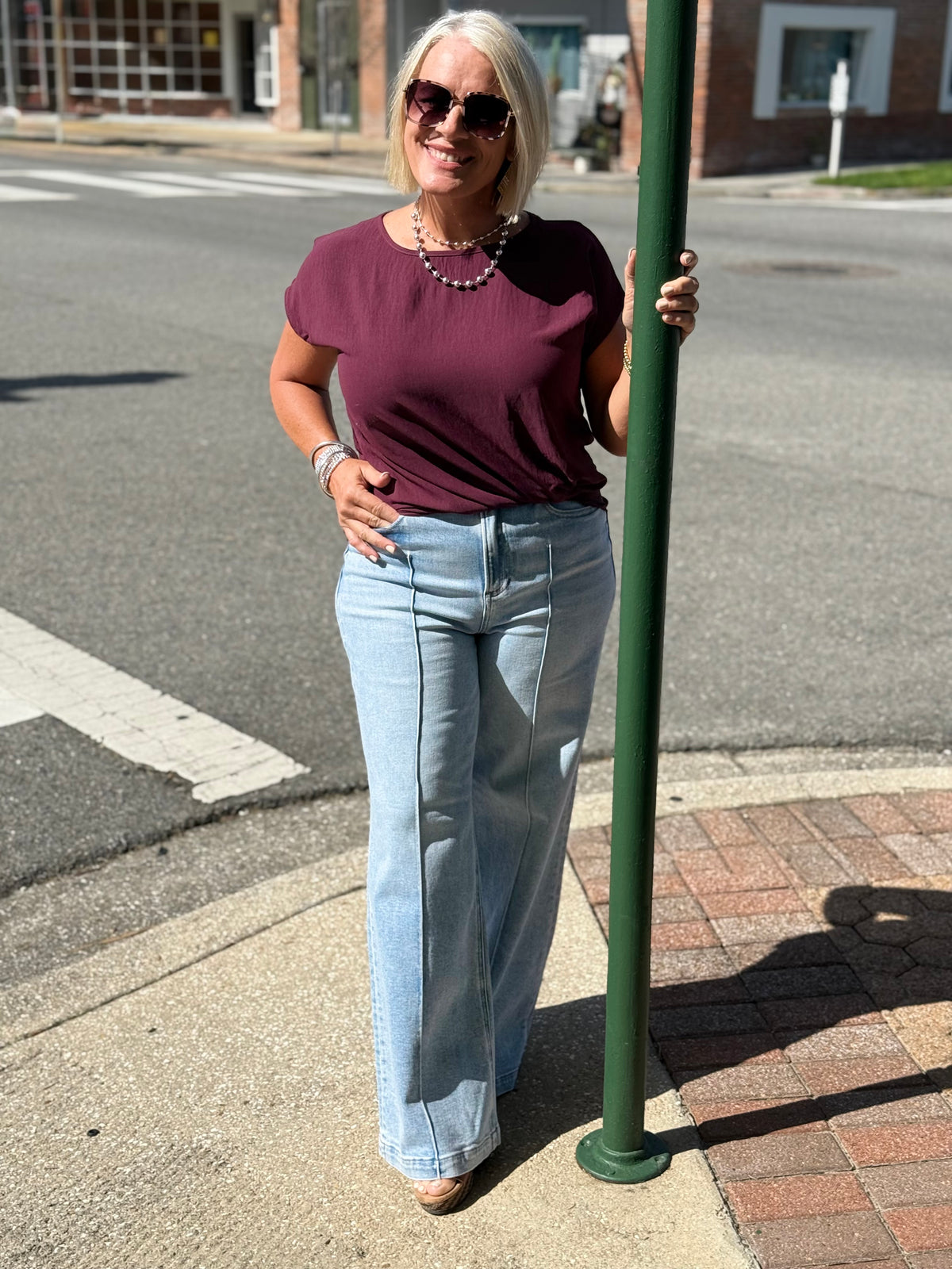 Model wearing a rich raisin Side Twist Hem Short Sleeve Top with light blue wide-leg jeans, standing outdoors.