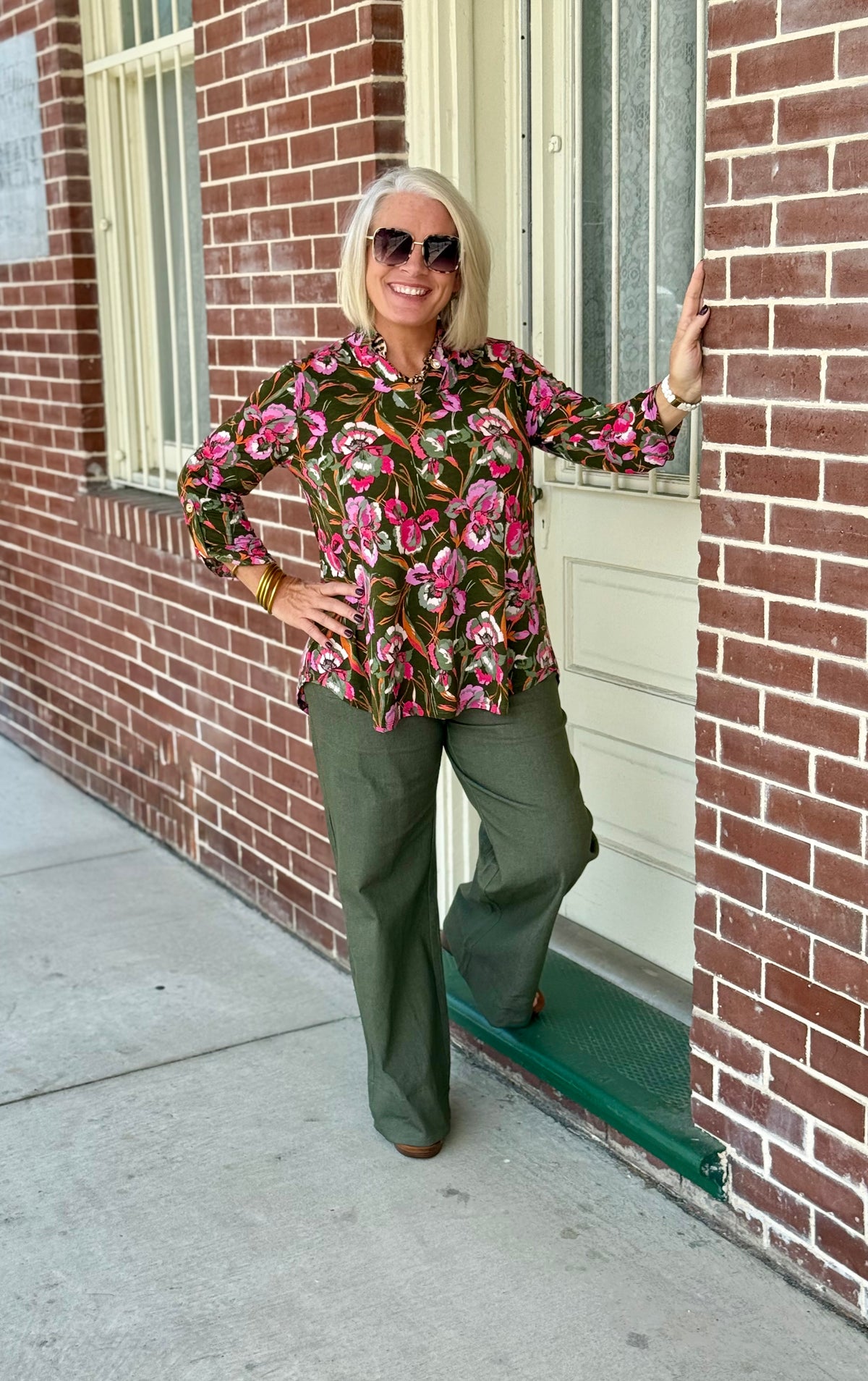 Dark olive blouse with pink and green floral pattern, ruffled collar, and 3/4 sleeves, styled with olive green pants.