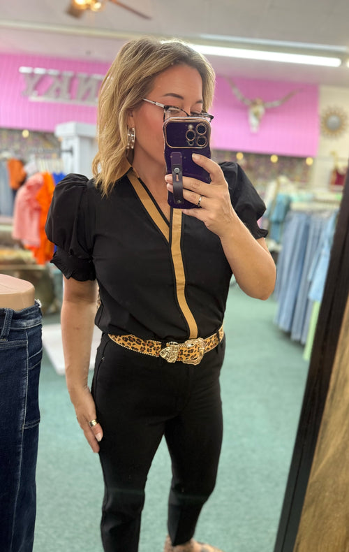 Black crinkled top with contrast accents, V-neck design, and puffed sleeves styled with fitted black pants and a leopard print belt.