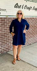 Navy A-line dress with ruffle neckline and 3/4 sleeves, featuring side pockets, styled with brown heeled shoes and accessories.