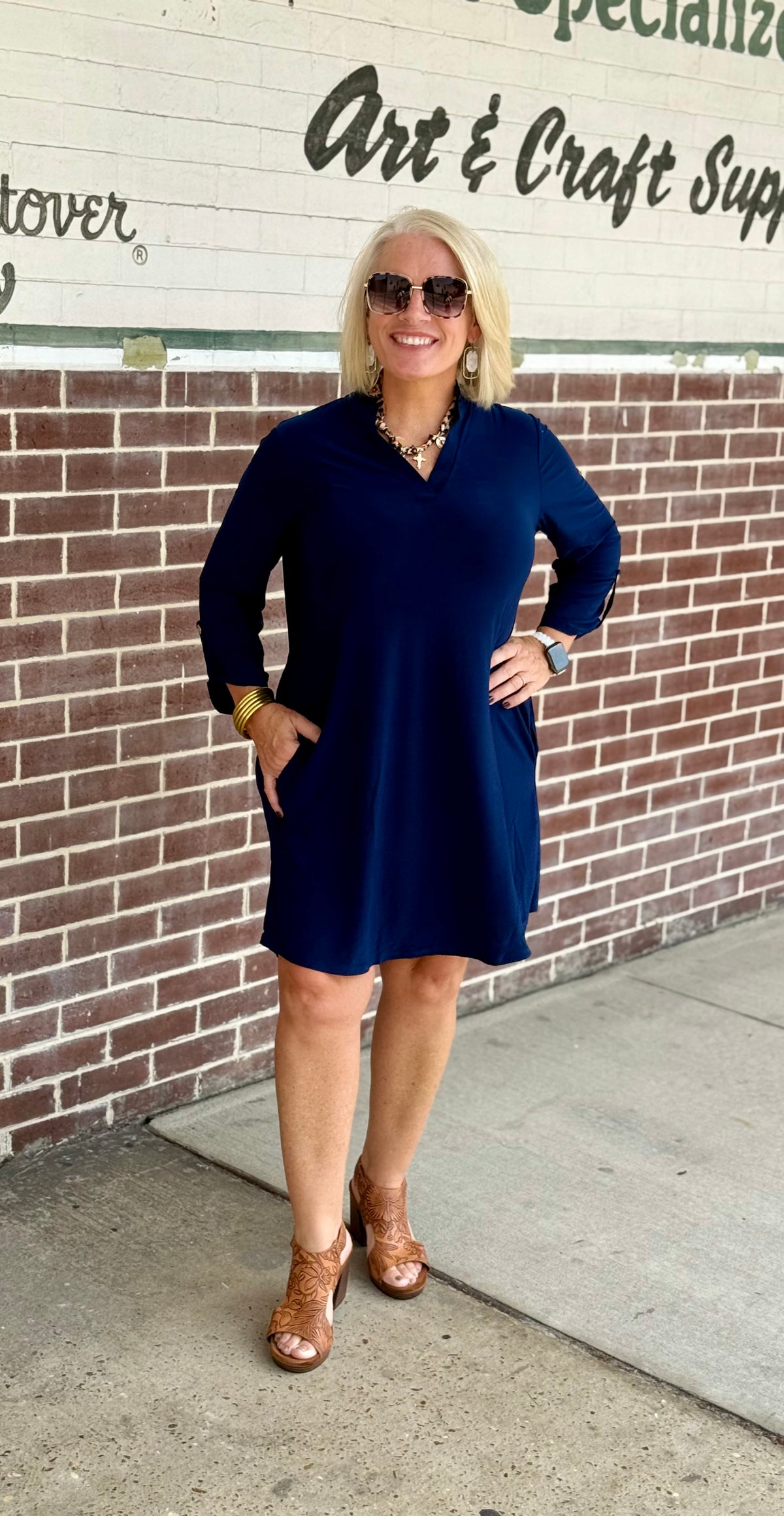 Navy A-line dress with ruffle neckline and 3/4 sleeves, featuring side pockets, styled with brown heeled shoes and accessories.