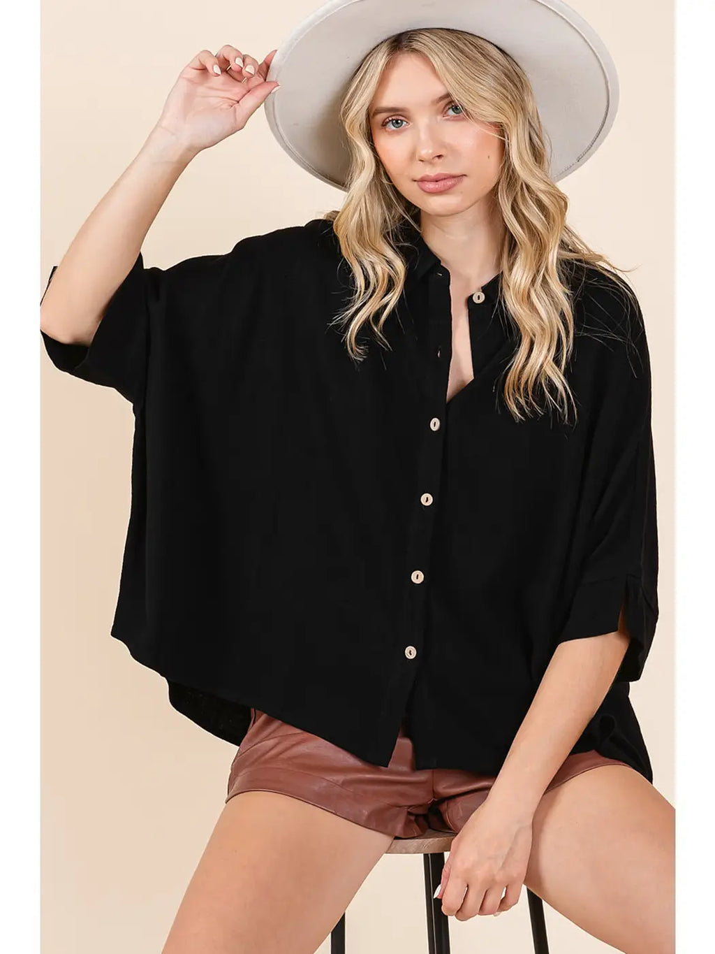 Black oversized button down shirt with a classic collar and cuffed short sleeves, styled casually with a hat and shorts.