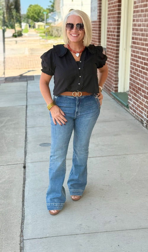 Black blouse with short puff sleeves and a Peter Pan collar, styled with high-waisted flared jeans and accessories outdoors.