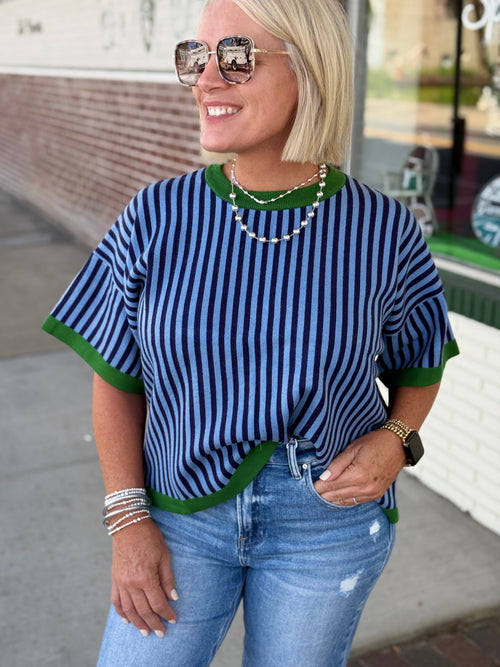 Bold blue and green striped short sweater top with green trim, styled with light blue jeans and accessories.