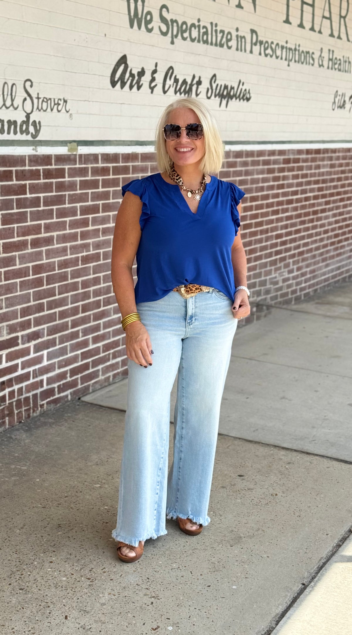 Model wearing a royal blue flutter sleeve top with a v-neckline, paired with light blue wide-leg jeans and accessories outdoors.
