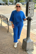 Model wearing a blue two-piece lounge set with a drop shoulder top and relaxed-fit pants, styled with white sneakers.