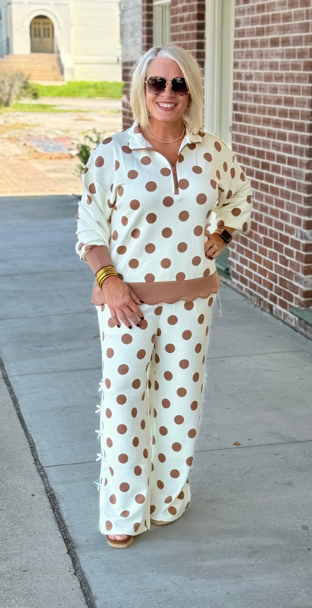 Cream polka dot outfit set featuring a three-quarter zip top and drawstring pants with scallop detailing, model outdoors.