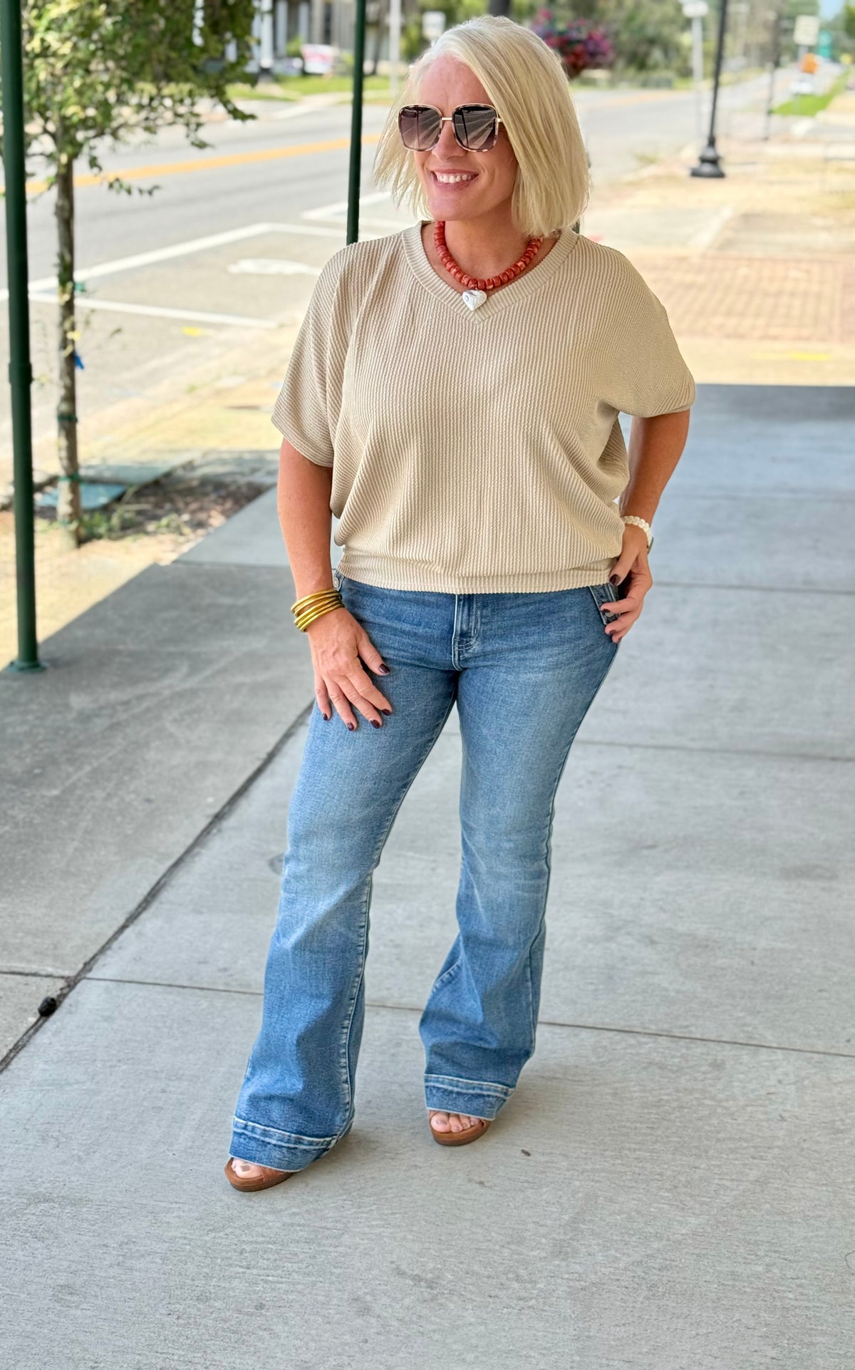 Taupe ribbed oversized top with V neckline and relaxed fit, styled with blue jeans and accessories outdoors.