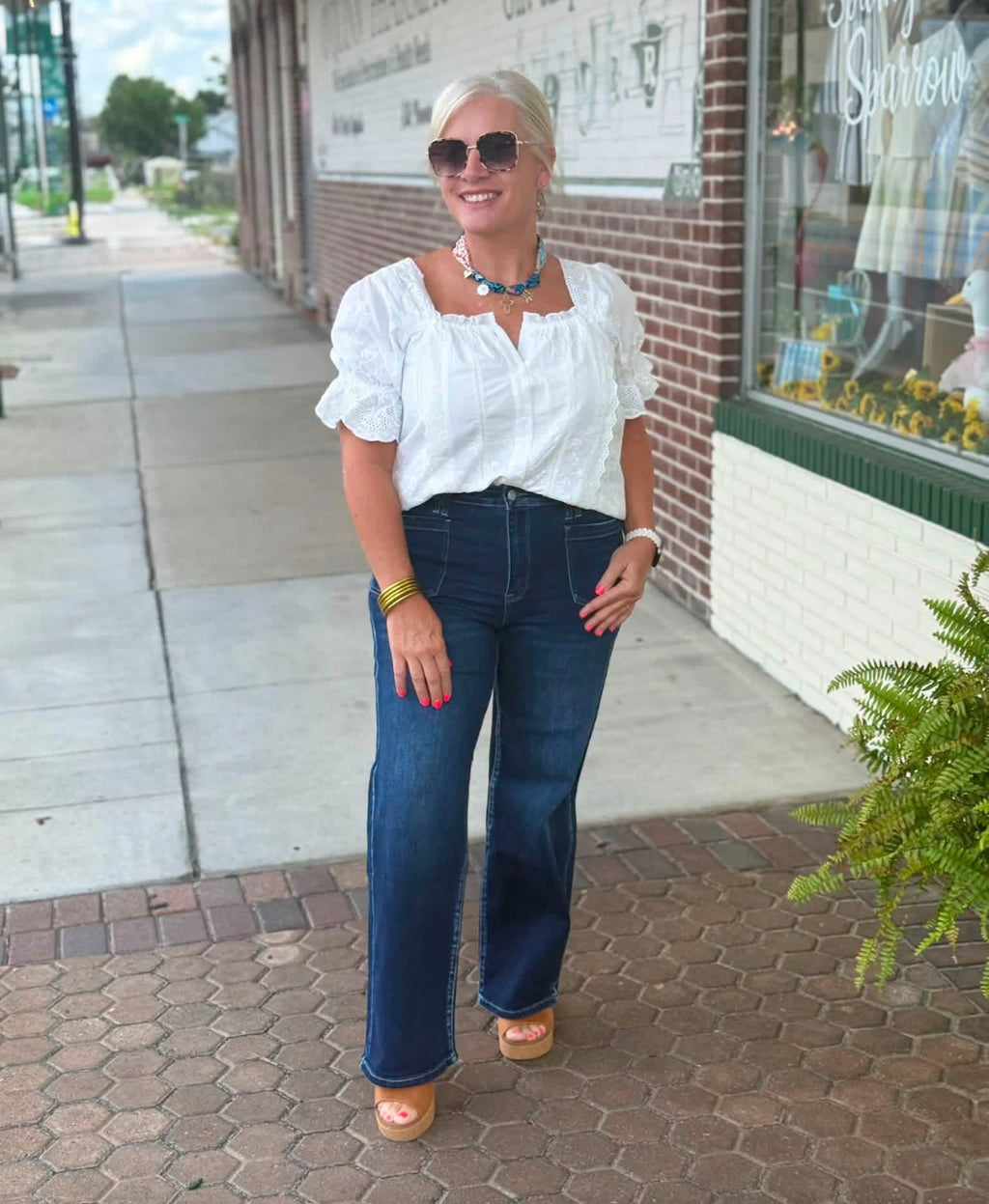 White square neck eyelet blouse with short puff sleeves, styled casually with high-waisted jeans and platform sandals.