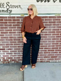 Rust 3/4 sleeve button-down blouse styled with dark pants and accessories against a brick wall.