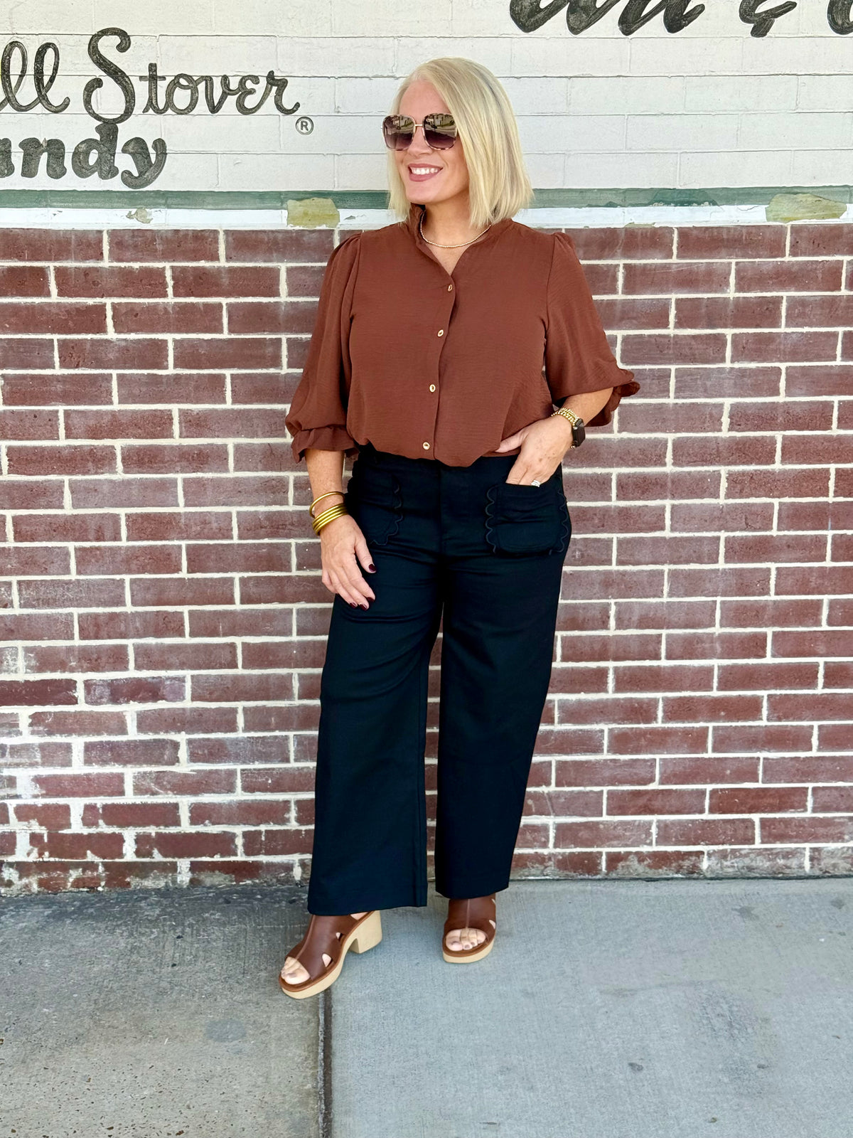 Rust 3/4 sleeve button-down blouse styled with dark pants and accessories against a brick wall.