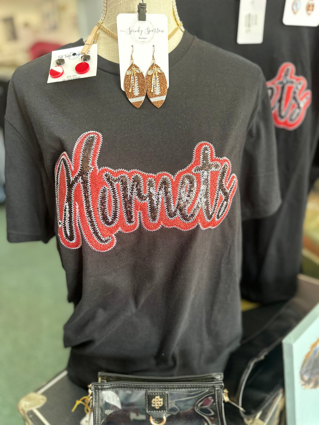 Black short sleeve T-shirt with sequined 'Hornets' design in red and silver, displayed on a mannequin with accessories.