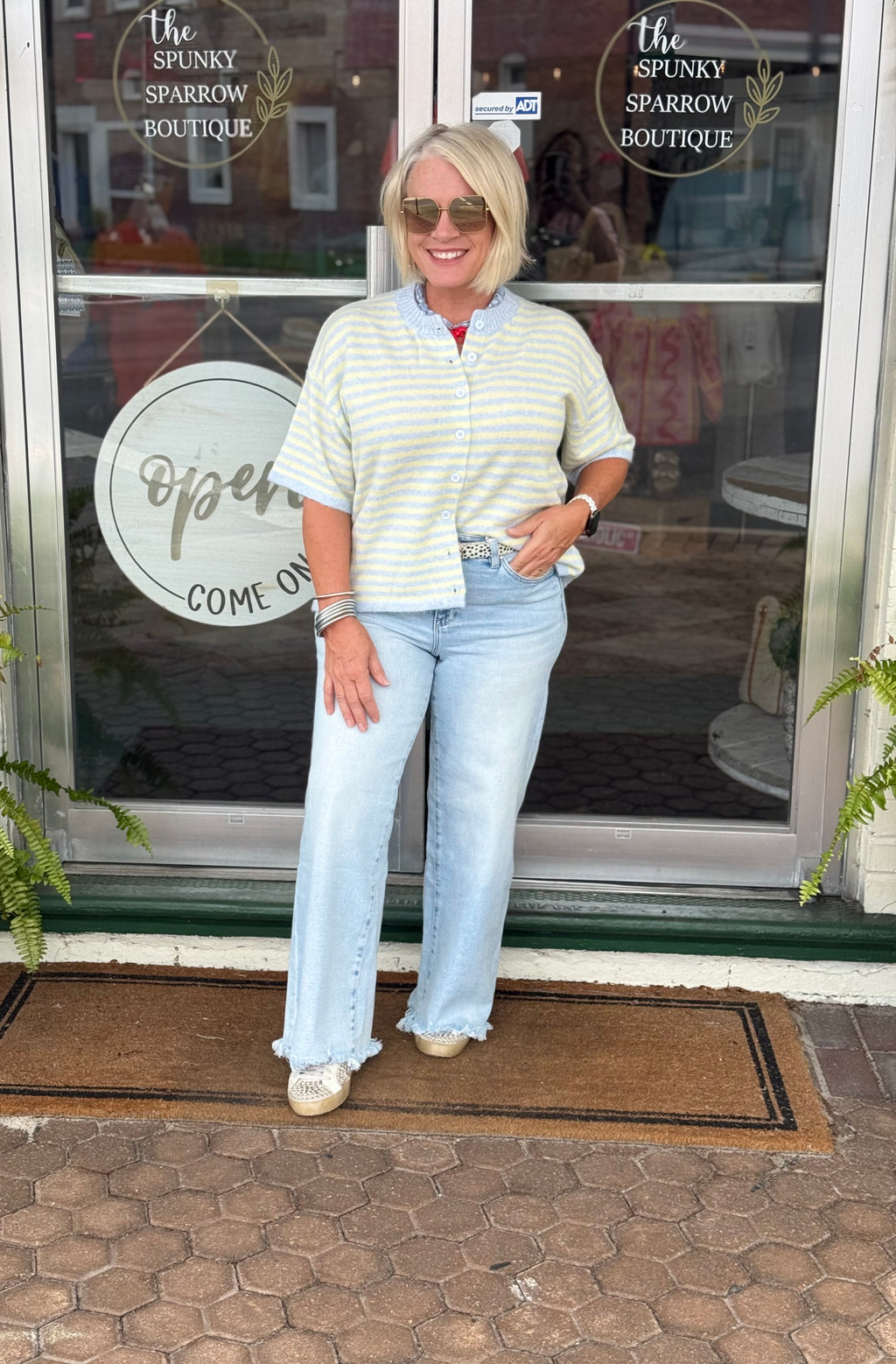 Light blue and yellow striped short sleeve cardigan worn open, featuring a ribbed round neckline and relaxed fit.