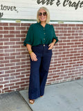 Model wearing a hunter green 3/4 sleeve button-down blouse styled with high-waisted wide-leg pants against a brick wall.