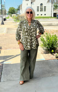 Dark olive blouse with floral pattern and smocked sleeves, styled with wide-leg trousers outdoors.
