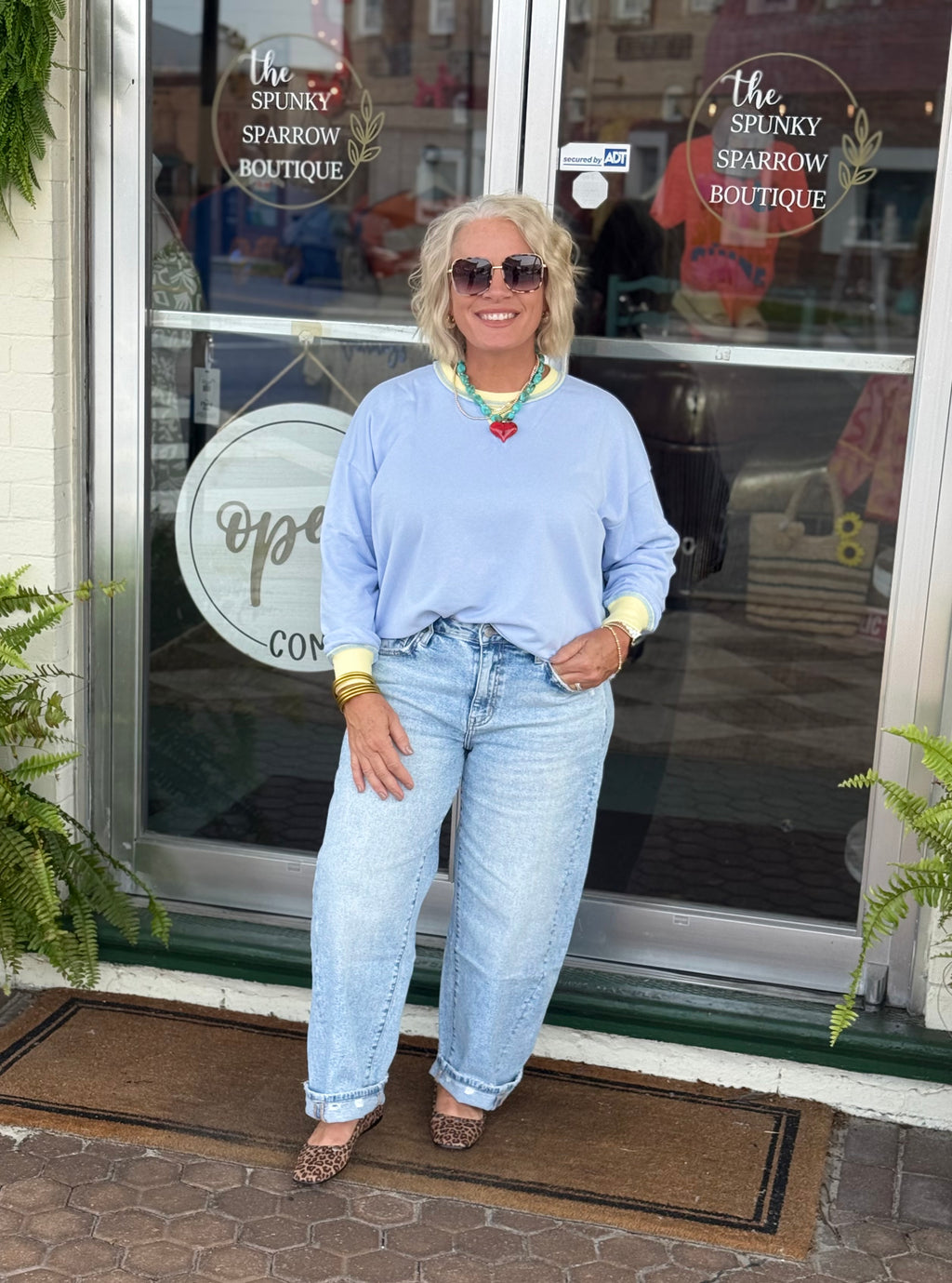 Person wearing a sky blue long sleeve pullover top with contrast trim, paired with light blue jeans outside a boutique.