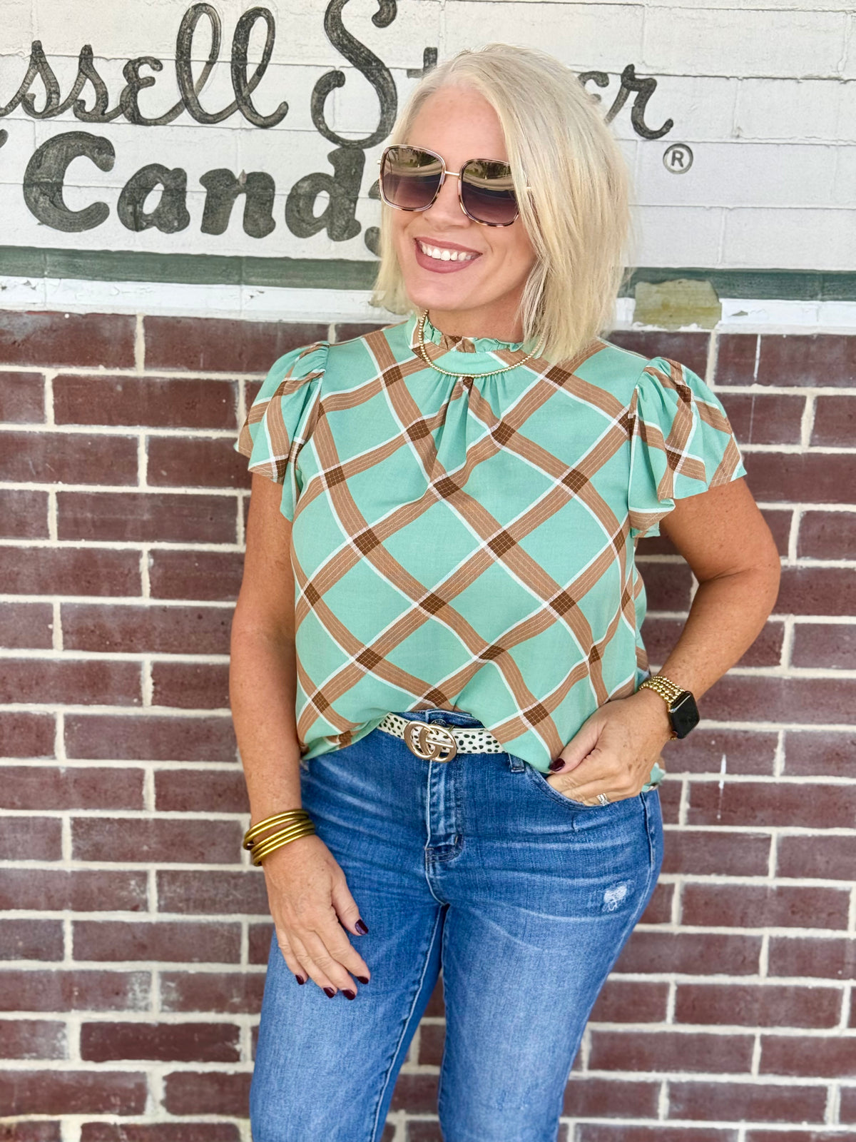 Sage plaid blouse with ruffle sleeves and round neckline, styled with blue jeans.
