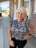 Model wearing the Savanna Stripe Top with bold zebra print and a functional tie neckline, styled with black pants outdoors.