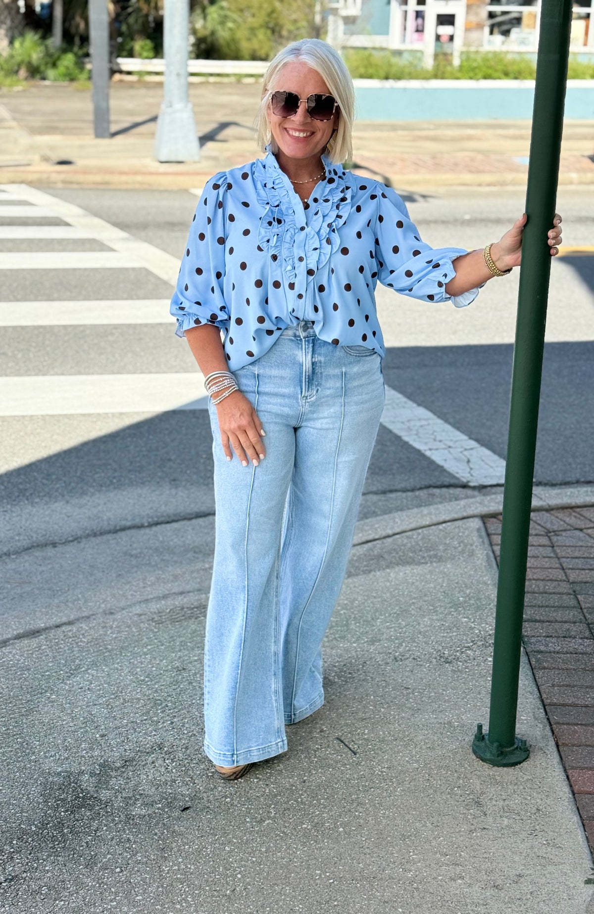Blue polka dot ruffle blouse styled with light blue wide-leg jeans in an outdoor setting.