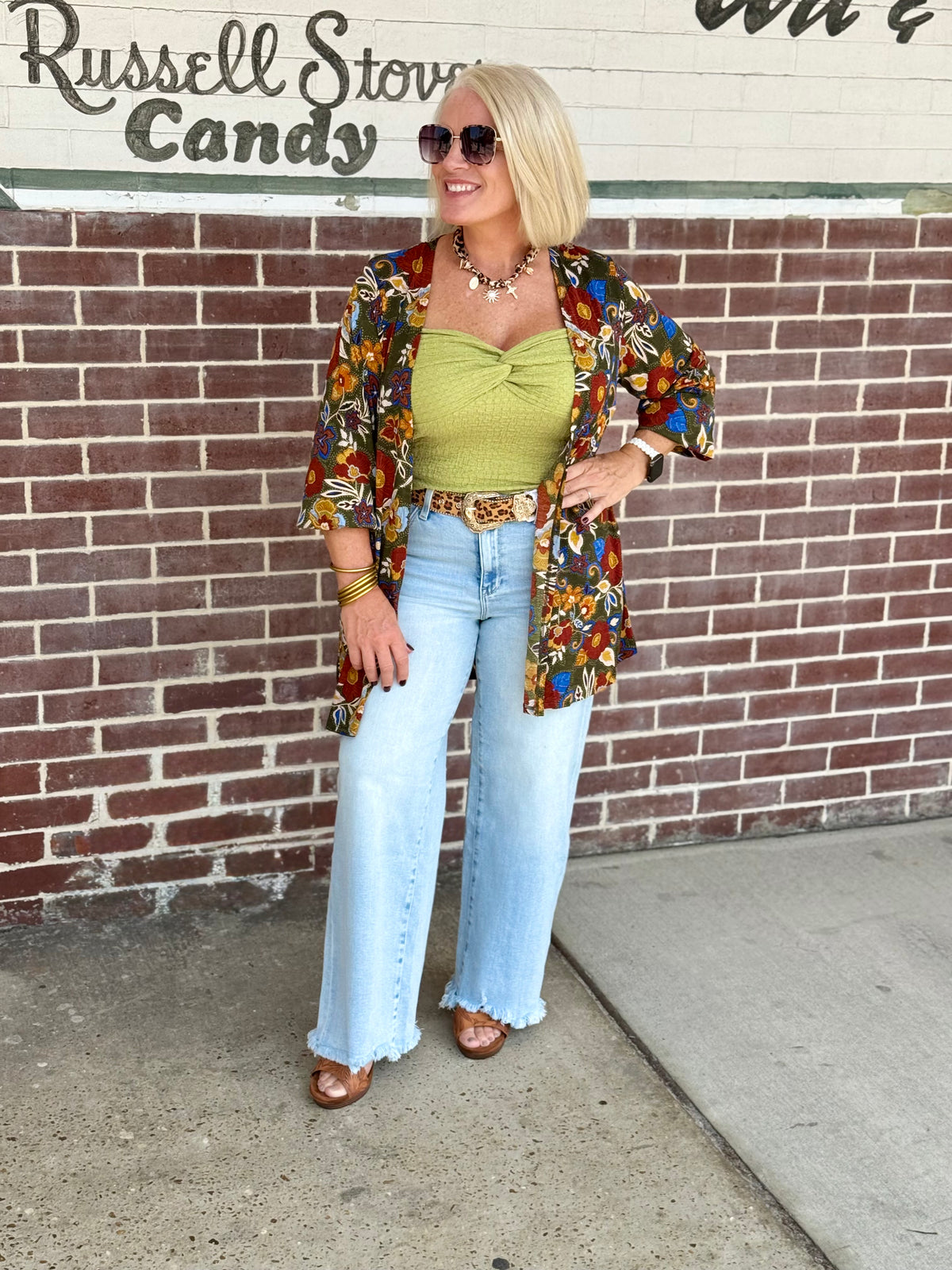 Person wearing a flowy open front cardigan with smocked sleeves and a colorful floral pattern, paired with light blue wide-leg jeans.