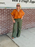 Olive high-rise wide-leg pants with front pockets, styled with a loose top and brown shoes, accessorized with sunglasses.