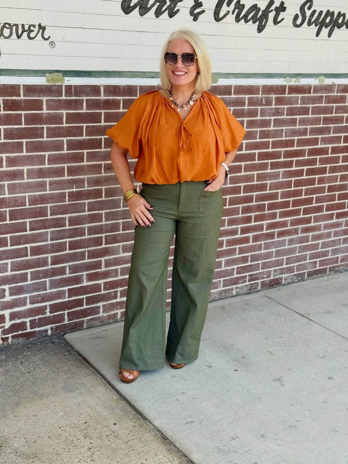Olive high-rise wide-leg pants with front pockets, styled with a loose top and brown shoes, accessorized with sunglasses.