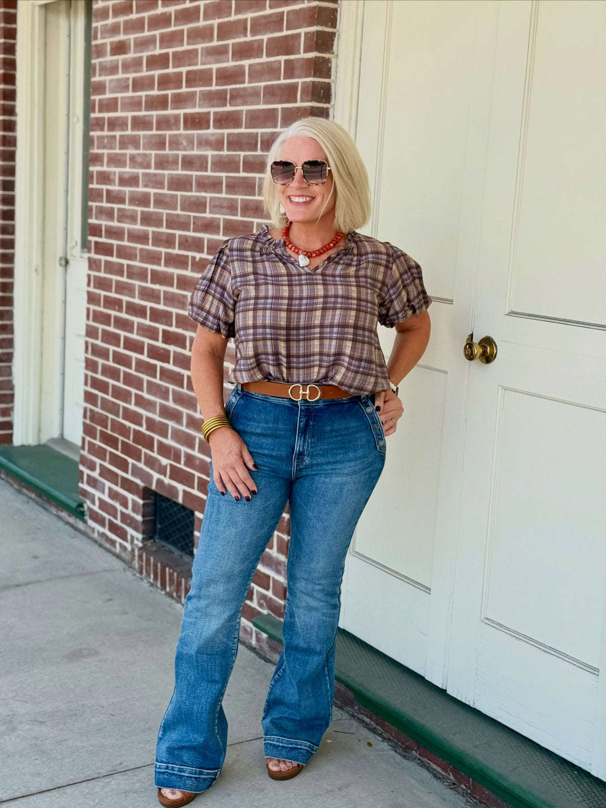 Model wearing a plaid puff sleeve blouse with a ruffle neckline, styled with high-waisted flared jeans and accessories.